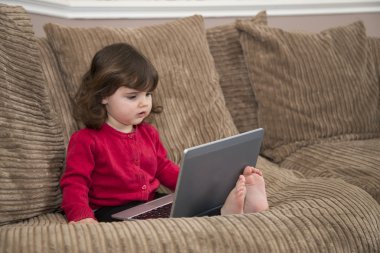 Genç kız kanepede dizüstü bilgisayar kullanarak