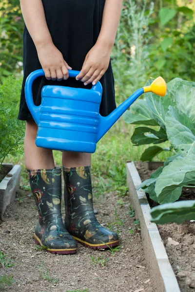 La bambina in giardino con l'annaffiatoio blu . — Foto Stock