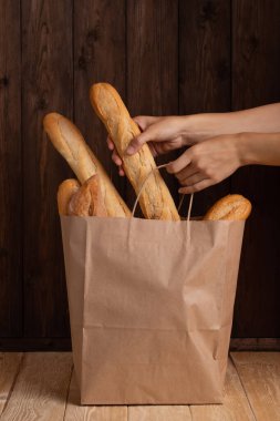 Hands Of Young Woman Takes Fresh Breads Bought In Store From Paper Bag Close Up. Traditional Baguette