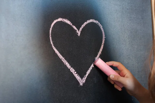 On Chalk Board Drawing Heart With Pink Chalk In Child Hand Close Up.