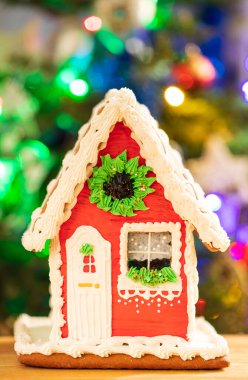 Bright Colorful Christmas Gingerbread House On Wooden Table On Background Of Christmas Tree With Burning Garlands Close Up.
