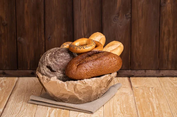 ボウルに新鮮なロシアの素朴なパンは 質感と木製の背景にナプキンにライトブラウンクラフト紙で包まれています — ストック写真