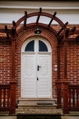 Klasik ahşap oyma oval kapı, cam takılı, verandanın üzerinde kahverengi gölgelik ve lamba, kırmızı tuğla duvar, iskan dairesinin girişi, Veltrusy kalesi, Çek Cumhuriyeti, 22 Kasım 2020