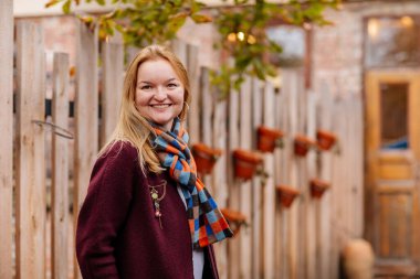 Sonbahar zamanı açık havada sıcak palto ve renkli eşarp giyen zarif genç bir kadının portresi. Kadın poz veriyor, çitlere yaslanıyor. Bulanık şehir geçmişi. Seyahat tutkusu kavramı.