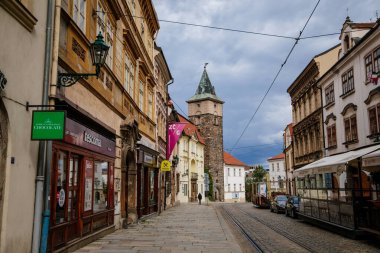 Güneşli bir günde Plzen 'in merkezinde renkli tarihi binalar bulunan dar bir caddenin sonundaki ortaçağ kara gotik su kulesi, Pilsen, Batı Bohemya, Çek Cumhuriyeti, 29 Mayıs 2021