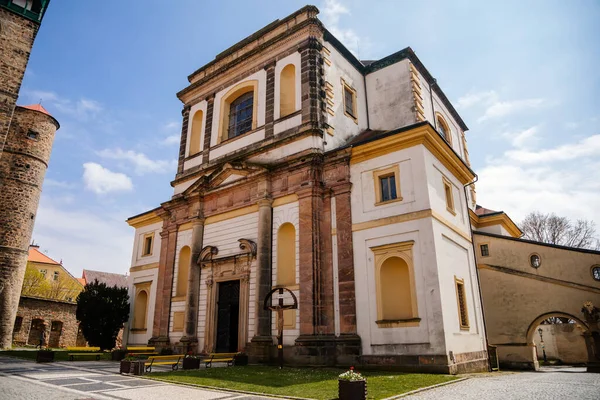Barok ve neoklasik stil St. James Kilisesi güneşli bir günde, sarı banklar ve çiçekler, tarihi merkez, Bohemya Cenneti veya Cesky Raj, Jicin, Çek Cumhuriyeti, 1 Mayıs 2021