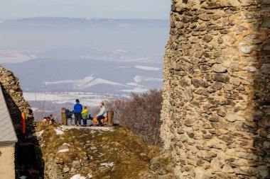 Aile bankta, anne baba çay, panoramik manzara, ortaçağ gotik kalesi Kostomlaty veya Sukoslav, kar, tepede taş yıkıntısı, güneşli kış günü, Çek Cumhuriyeti, 20 Şubat 2021