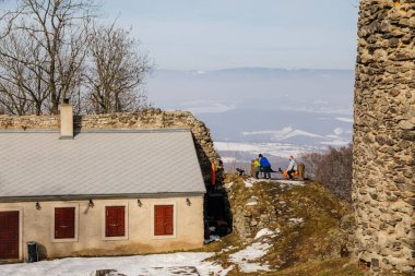 Aile bankta, anne baba çay, panoramik manzara, ortaçağ gotik kalesi Kostomlaty veya Sukoslav, kar, tepede taş yıkıntısı, güneşli kış günü, Çek Cumhuriyeti, 20 Şubat 2021