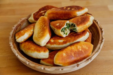 Yeşil soğanlı ve yumurtalı leziz kızarmış turtalar, köfteler veya pirozhki, geleneksel Rus hamur işi mutfağı, ev yapımı kekler, ahşap arka planda beyaz tabak, yiyecek Slavonik konsepti, kırsal köy