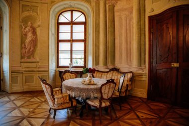 Rokoko şatosu, oyulmuş ahşap mobilya, koltuk ve kanepe, çay için hazırlanan masa, porselen tabaklar, örülmüş dantel masa örtüsü, vazoda kırmızı güller, Barok kalesi Steknik, Çek Cumhuriyeti, 19 Haziran 2021