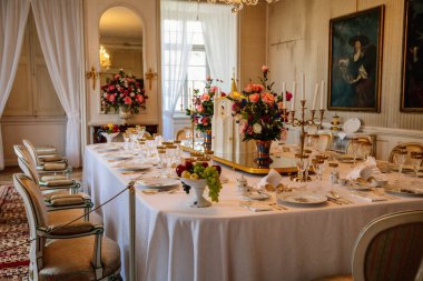Krasny Dthe Chateau, Kuzey Bohemya, Çek Cumhuriyeti, 19 Haziran 2021: Kale içi, yemek odasında barok mobilyalar, akşam yemeği, şarap kadehleri, beyaz masa örtüsü üzerinde porselen servis edilen büyük masa.