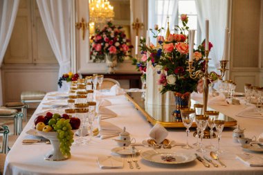 Krasny Dthe Chateau, Kuzey Bohemya, Çek Cumhuriyeti, 19 Haziran 2021: Kale içi, yemek odasında barok mobilyalar, akşam yemeği, şarap kadehleri, beyaz masa örtüsü üzerinde porselen servis edilen büyük masa.