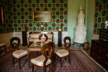 Krasny Dthe Chateau, Kuzey Bohemya, Çek Cumhuriyeti, 19 Haziran 2021: Kale içi, Biedermeier mobilyaları ahşap oymalı sandalyeler, antika beyaz seramik kaplama ocak.