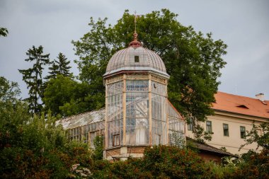 Valec, Batı Bohemya, Çek Cumhuriyeti, 19 Haziran 2021: Botanik bahçesindeki cam ve çelik sera yakınlarındaki yeşil ağaçlar, yaz günü Barok kalesinin yanındaki parkta tarihi köşk.