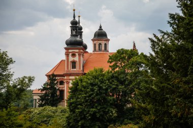 Valec, Batı Bohemya, Çek Cumhuriyeti, 19 Haziran 2021: Güneşli yaz gününde şatosu yakınlarında kuleleri olan Kutsal Üçlü 'nün Barok kırmızı ve sarı kilisesi.