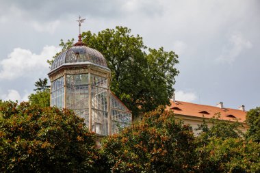 Valec, Batı Bohemya, Çek Cumhuriyeti, 19 Haziran 2021: Botanik bahçesindeki cam ve çelik sera yakınlarındaki yeşil ağaçlar, yaz günü Barok kalesinin yanındaki parkta tarihi köşk.