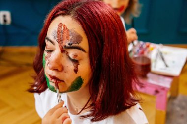 Aile eğlencesi ev konsepti. Anne ve küçük kızı resim çiziyor, boya fırçaları ve suluboya boya kullanarak eğleniyorlar. Çocuklar ve ebeveynler birlikte resim yapıyor, yüzlerinde suluboya, ev karantinası.