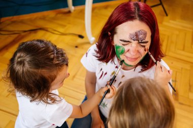 Aile hobileri boş zaman aktiviteleri ev konsepti. Anne ve küçük kızı, boya fırçaları ve suluboya boyalarla eğlenerek resim çiziyorlar. Çocuklar ve ebeveynler birlikte resim yapıyorlar, vücut boyası, ev karantinası..