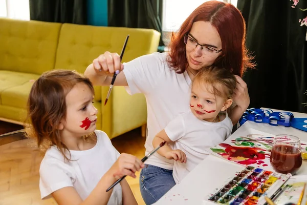Family hobbies leisure activity home concept. Mother and small daughter drawing with fun using paintbrushes and watercolors. Children and parent creating picture together, body paint, home quarantine.