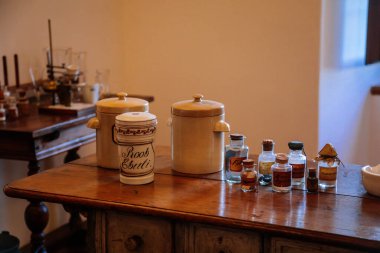 Kuks, Doğu Bohemya, Çek Cumhuriyeti, 10 Temmuz 2021: Barok hastanesi Kuks, tarihi eczanenin içi, ahşap masa ve rafta eski cam şişeler, tıbbi geçmiş, antika eczane.