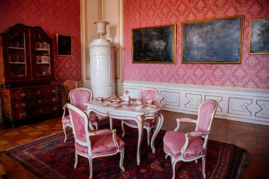 Valtice, Güney Moravya, Çek Cumhuriyeti, 04 Temmuz 2021: Barok mobilya, yemek odası veya beyaz seramik kaplama ocaklı pembe salon, masada porselen çay seti, yumuşak koltuklar.