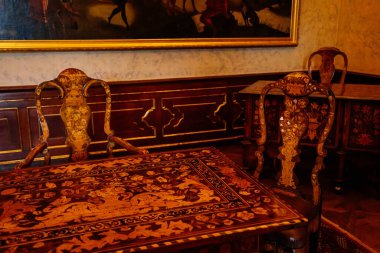 Valtice, Güney Moravya, Çek Cumhuriyeti, 04 Temmuz 2021: Barok ahşap oymalı mobilyalar, işlemeli masa ve sandalyeli kabine, altın çerçeveli resim.