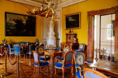 Valtice, Güney Moravya, Çek Cumhuriyeti, 04 Temmuz 2021: Barok ahşap oymalı mobilya, oyun odası veya beyaz seramik döşemeli soba, masalar, yumuşak sandalyeler ve koltuklu salon.