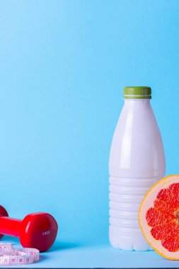 Minimalist diyet ve spor konsepti. Kırmızı dambıl, kefir şişesi, mavi arka planda şerit..