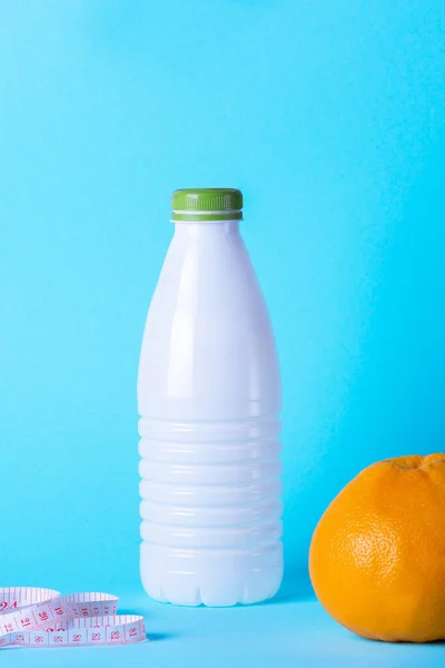 Minimalist diet and sports concept. Red dumbbell, kefir bottle, measuring tape on a blue background. Juicy grapefruit for a sports diet.