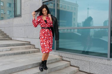 Şehir caddesinde poz veren zarif bir esmer kız. Şehrin arka planında şık giyinmiş güzel bir iş kadını..