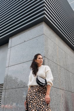 Şehir caddesinde poz veren zarif bir esmer kız. Şehrin arka planında şık giyinmiş güzel bir iş kadını..