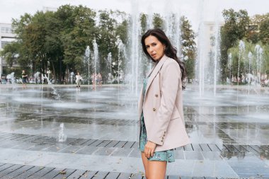 Şehir caddesinde poz veren zarif bir esmer kız. Şehrin arka planında şık giyinmiş güzel bir iş kadını..