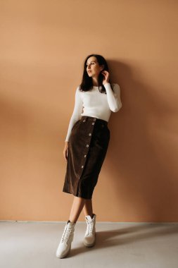 Genç zarif kız içeride poz veriyor. Duvarda ve pencerede zarif elbiseler içinde güzel bir iş kadını.