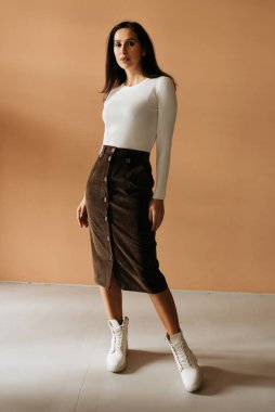 Genç zarif kız içeride poz veriyor. Duvarda ve pencerede zarif elbiseler içinde güzel bir iş kadını.