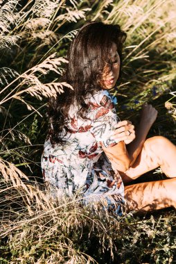 Zarif bir yaz elbisesi içinde genç ve güzel bir esmer ve güneş ışınlarında hasır şapkalı doğa yürüyüşünde.