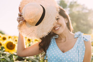 Zarif bir yaz elbisesi içinde genç ve güzel bir esmer ve güneş ışınlarında hasır şapkalı doğa yürüyüşünde.