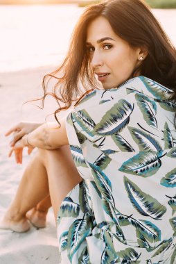 Zarif bir yaz elbisesi içinde genç ve güzel bir esmer ve güneş ışınlarında hasır şapkalı doğa yürüyüşünde.