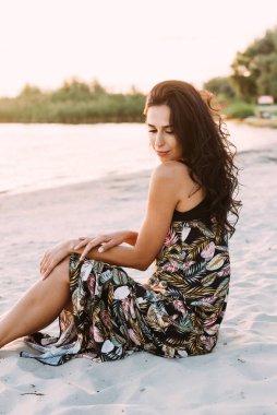 Zarif bir yaz elbisesi içinde genç ve güzel bir esmer ve güneş ışınlarında hasır şapkalı doğa yürüyüşünde.