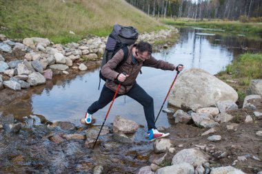 Turist varlıklı akış trekking direkleri kullanarak geçer