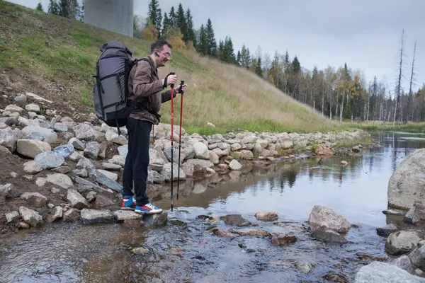 Turista passa fluxo afluente usando postes de trekking — Fotografia de Stock