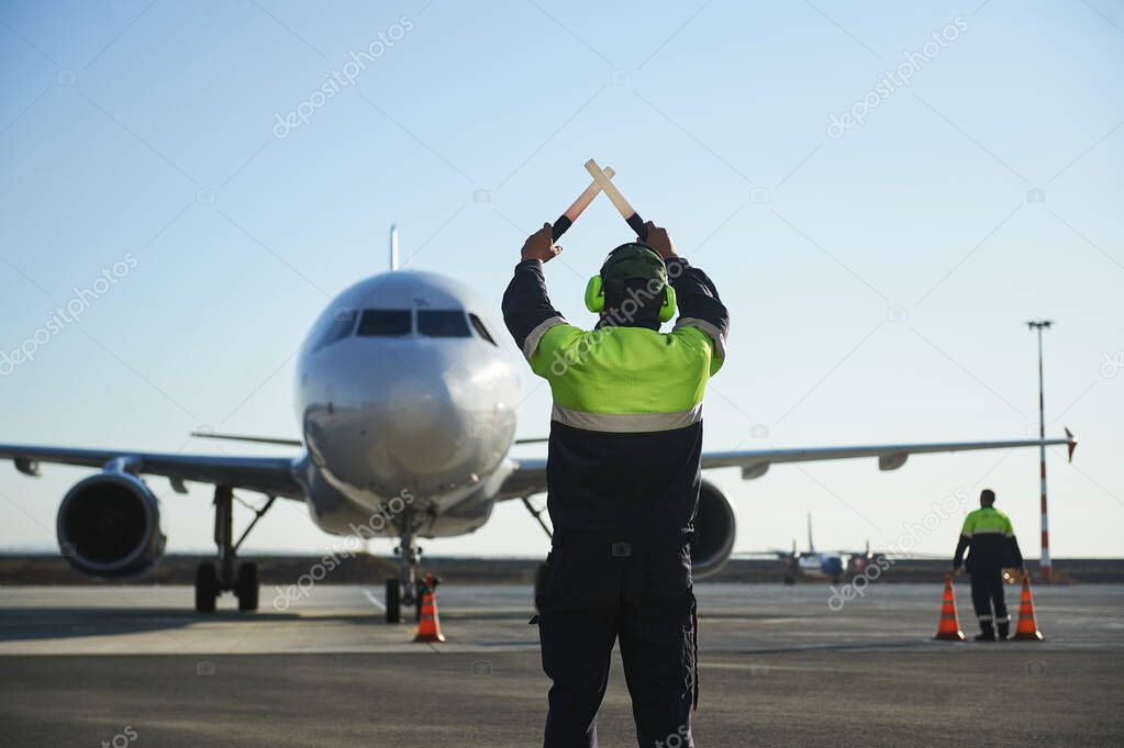 The runway traffic controller uses gestures and sticks to help the aircraft choose the correct trajectory around the airfield. Wearing a reflective vest