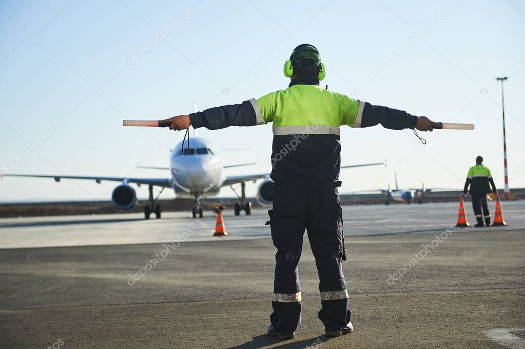 The runway traffic controller uses gestures and sticks to help the aircraft choose the correct trajectory around the airfield. Wearing a reflective vest