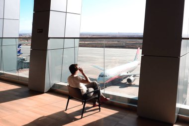 St. Petersburg, Rusya - 23 Ekim 2019: Havaalanı salonundaki büyük bir pencerede oturan bir kadın pisti izliyor. RED WING şirketinin uçakları         