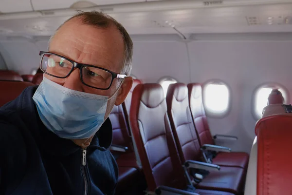 세에서 사이의 노인이 보호용 마스크와 안경을 착용하고 비행기의 객실에 있습니다 — 스톡 사진