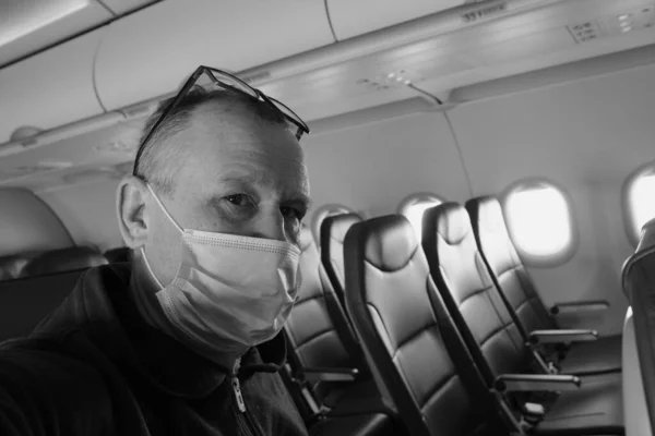 An elderly man 60-65 years old wearing a protective mask and glasses alone in the cabin of a passenger airliner. Empty seats - social distancing during the Covid-19 coronavirus pandemic