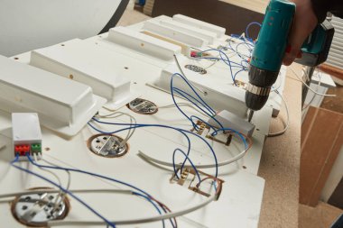 Bir katılımcı, mobilyanın elektrik kısmını fabrikanın atölyesinde monte eder. Kablolar, diyagram, vida vidası, elektrikçi, tornavida.