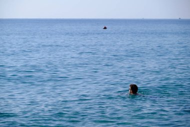 25-30 yaşlarında bir adam denizde, güneş gözlükleriyle, yüzeyde sadece bir baş, esmer, kalın saçlı, yakışıklı..