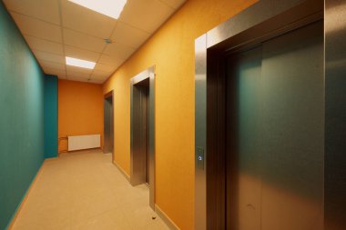 Sıradan bir apartman koridoru, parlak renklerle boyanmış, metal isimsiz apartman kapıları, zengin gölgeler.