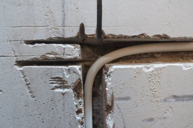 Öğütücü tarafından yapılmış bir oyukta bir dairenin beton duvarına elektrik kablosu döşeme örneği. Beyaz yalıtılmış bakır tel, alçıyla örülmeye hazır..