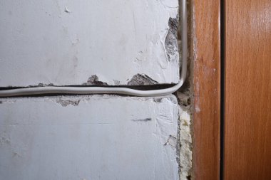 Öğütücü tarafından yapılmış bir oyukta bir dairenin beton duvarına elektrik kablosu döşeme örneği. Beyaz yalıtılmış bakır tel, alçıyla örülmeye hazır..